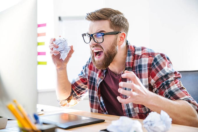 Angry crazy modern designer in glasses with beard yelling and crumpling paper on his workplace